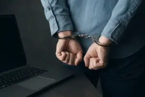 Handcuffed individual near laptop, symbolising CoinDCX crypto hack investigation involving malware and internal security breach.