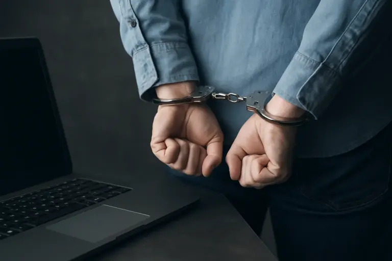 Handcuffed individual near laptop, symbolising CoinDCX crypto hack investigation involving malware and internal security breach.