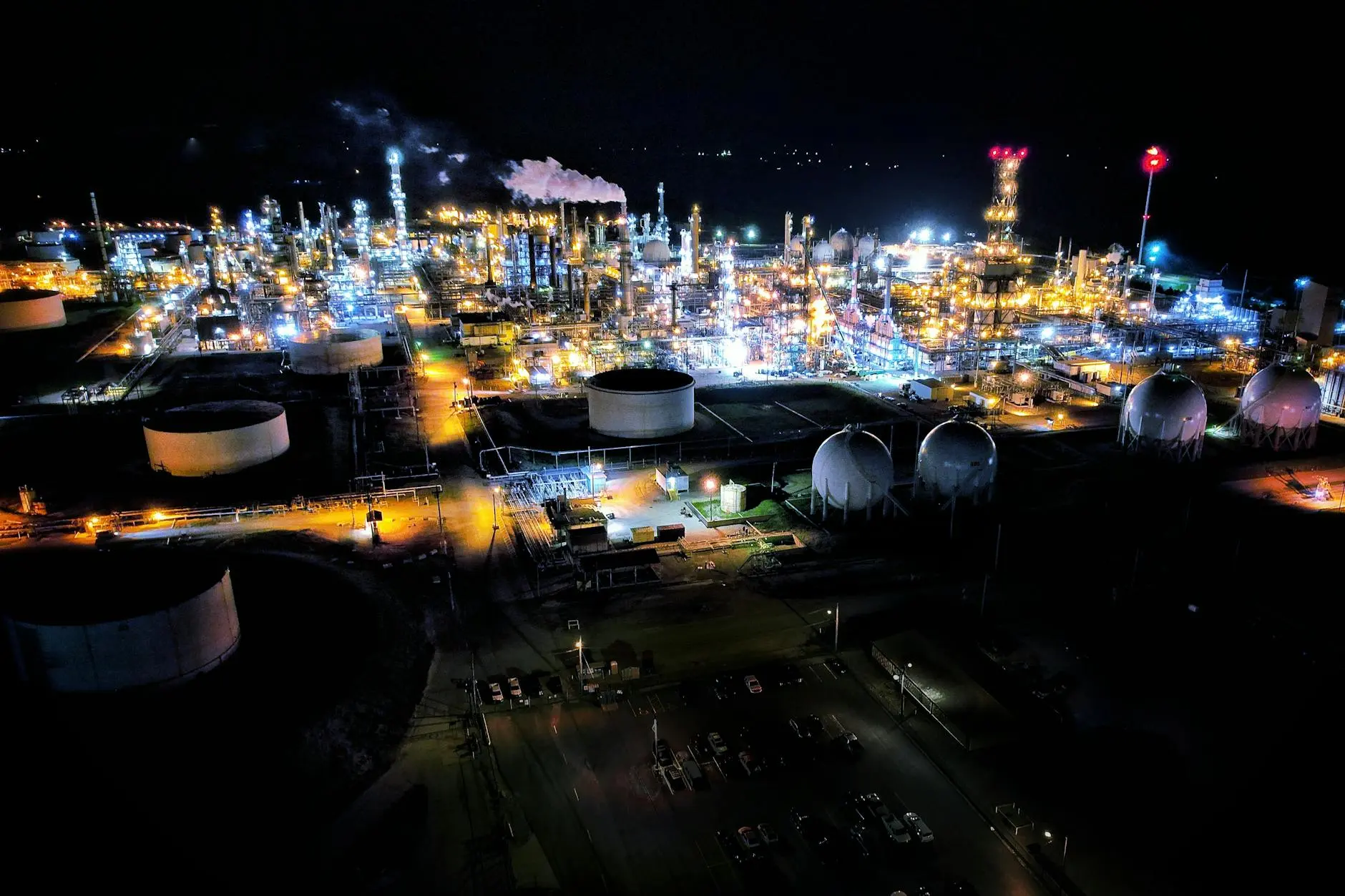 Aerial view of a brightly lit crude oil refinery plant at night.