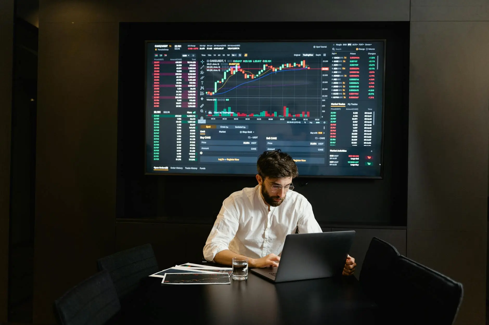 Trader analyzing cryptocurrency data on a laptop in a trading room.