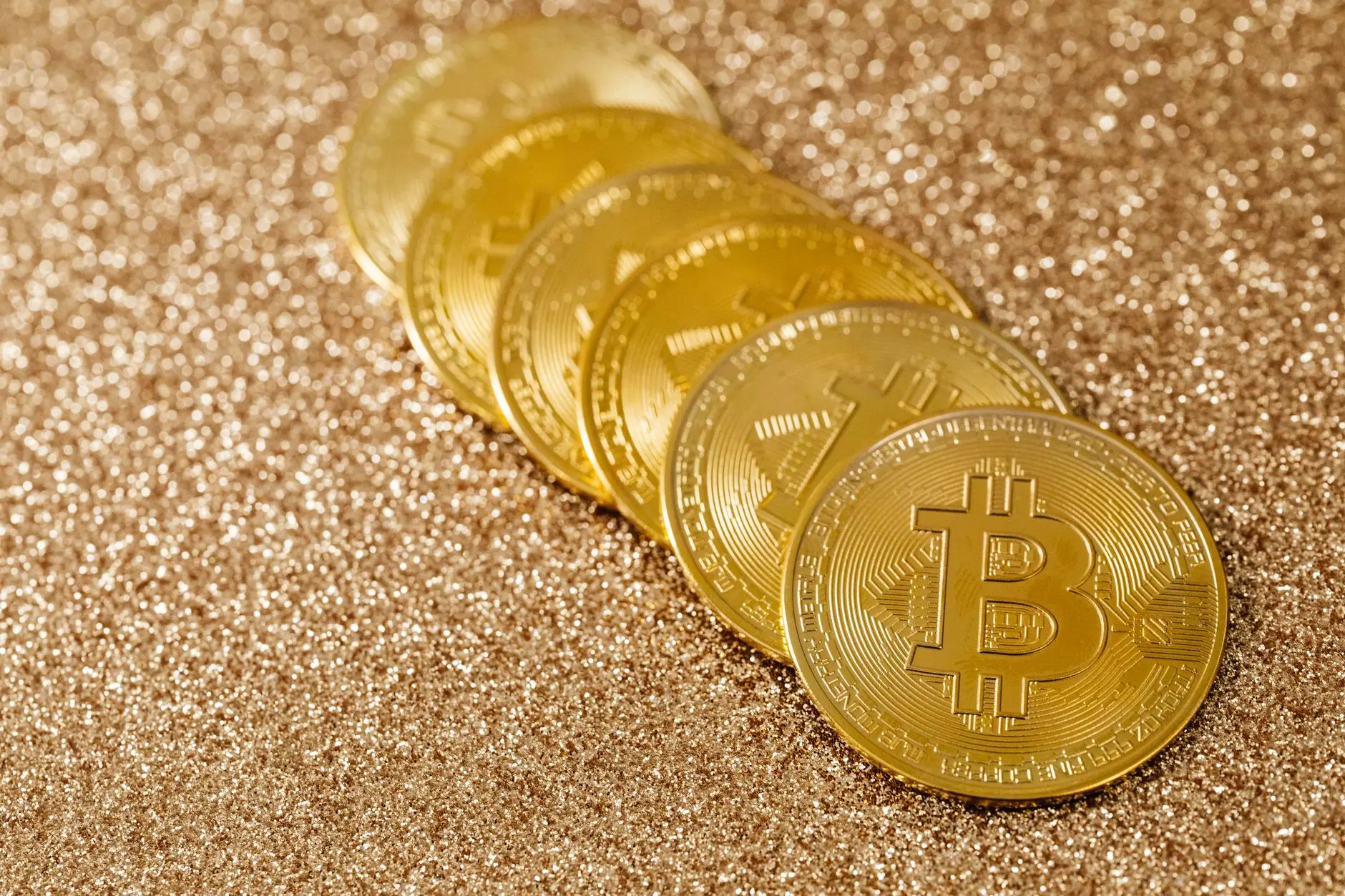 Five golden Bitcoin coins displayed on a glittering surface.
