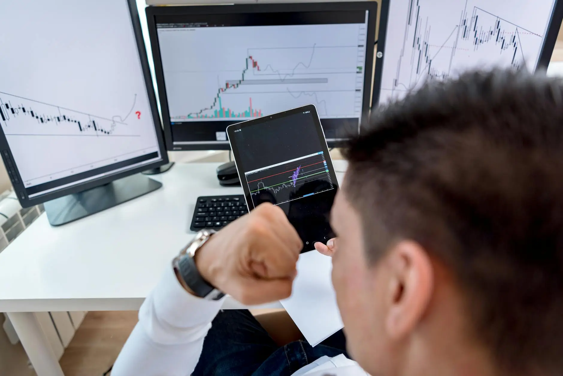 Young trader anxiously monitoring financial charts on multiple screens.