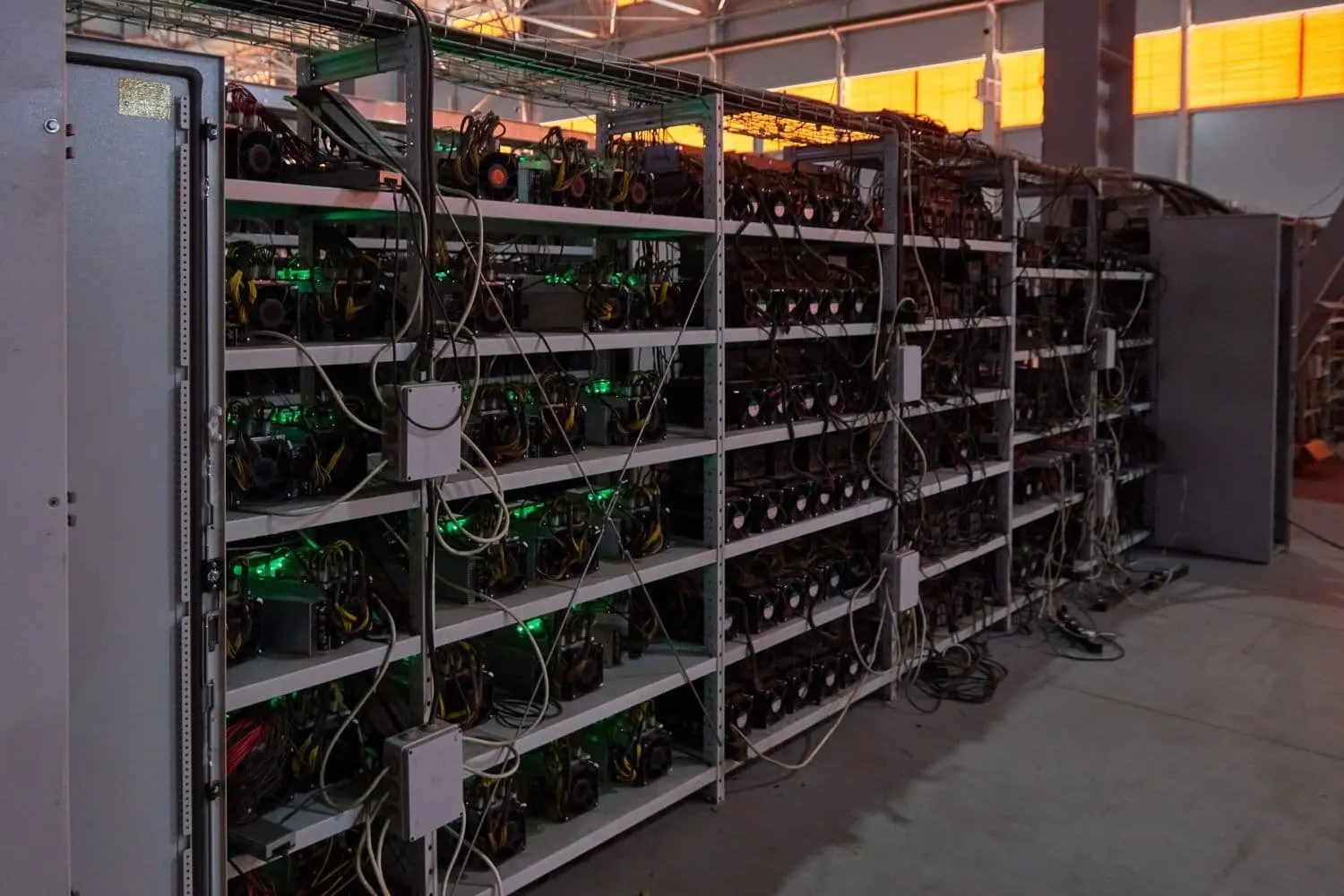Rows of professional Bitcoin ASIC mining rigs with cooling fans and cables in a warehouse facility