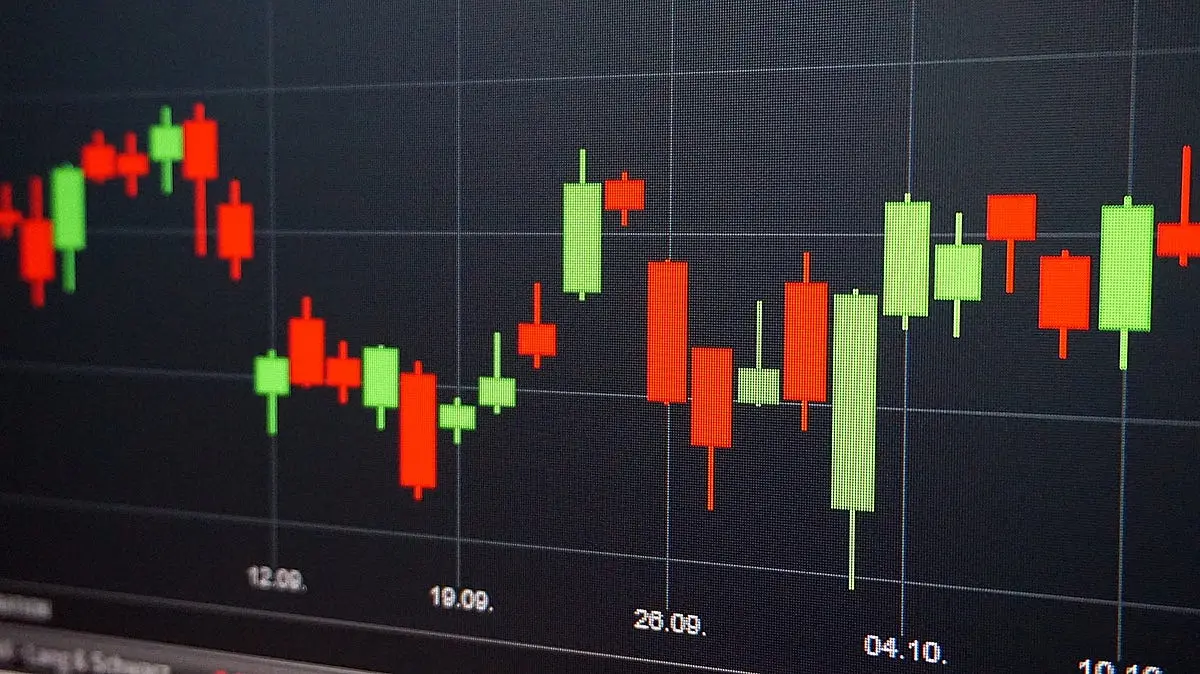 Close-up of a digital screen showing red and green candlestick price charts on a dark grid background