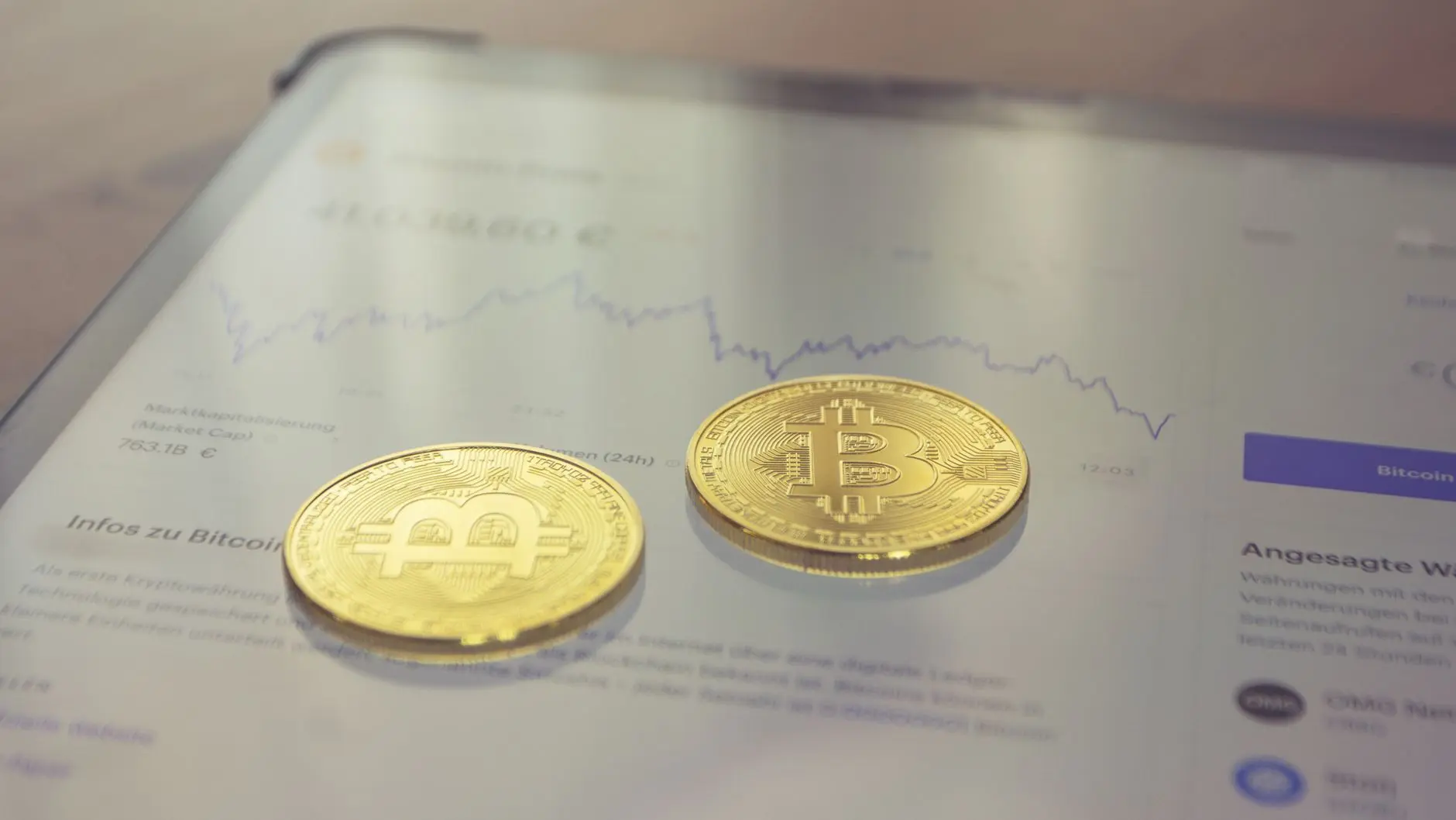 Two gold Bitcoin coins on a smartphone displaying cryptocurrency market data.