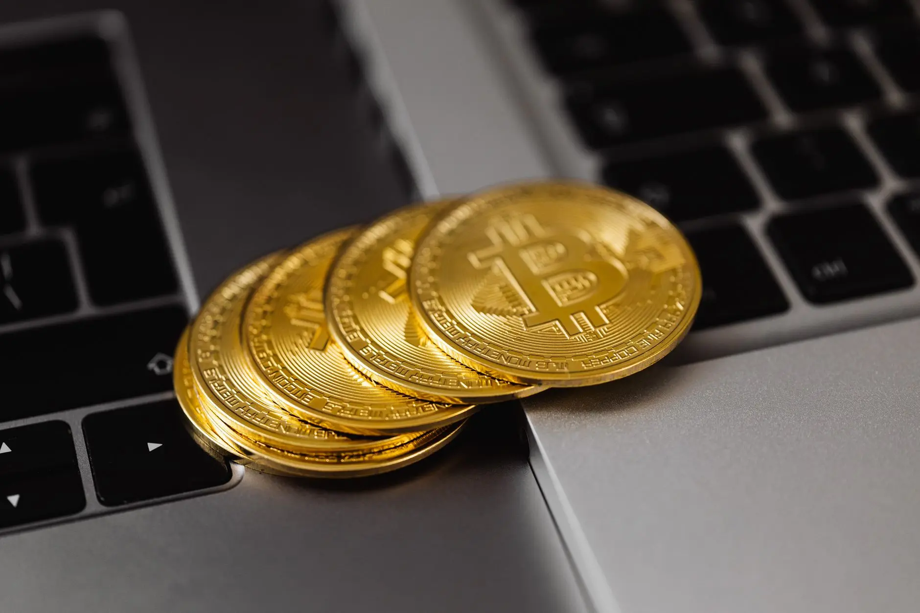 Stack of gold Bitcoin coins resting on a laptop keyboard.