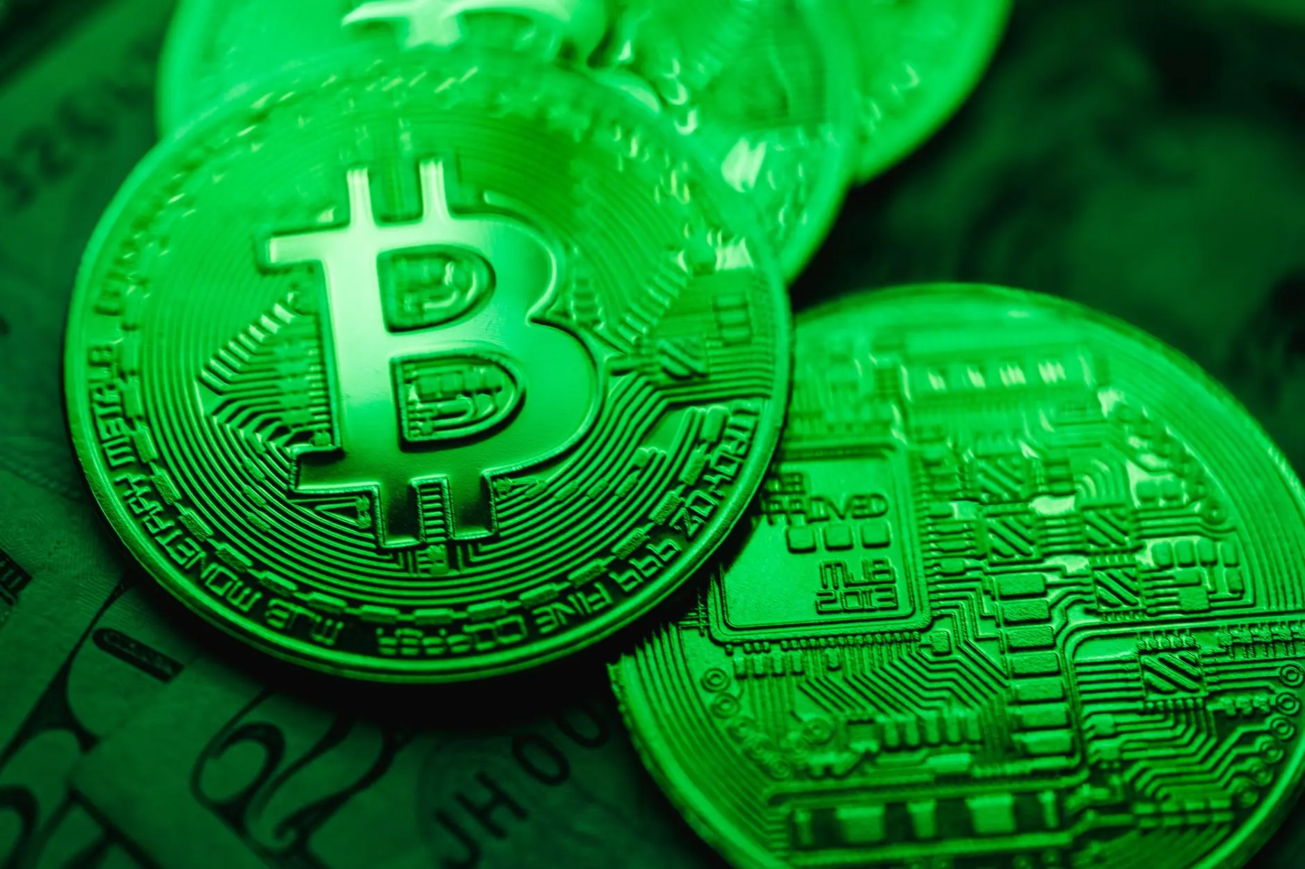 Close-up of Bitcoin coins with a green hue and visible circuit patterns.