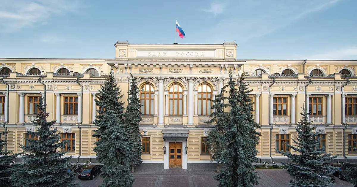 Facade of the Central Bank of Russia in Moscow with flag and trees.