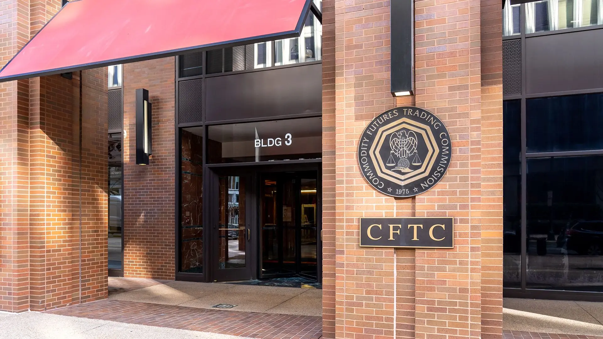 Entrance of the Commodity Futures Trading Commission building featuring the CFTC seal and sign on a brick wall.