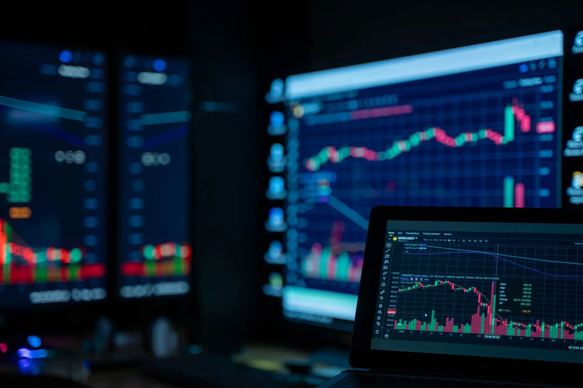 Multiple computer screens displaying cryptocurrency trading charts in a dark setting.