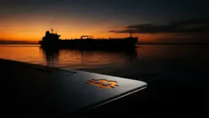 Oil tanker silhouette at dusk with Bitcoin symbol on dark metallic surface