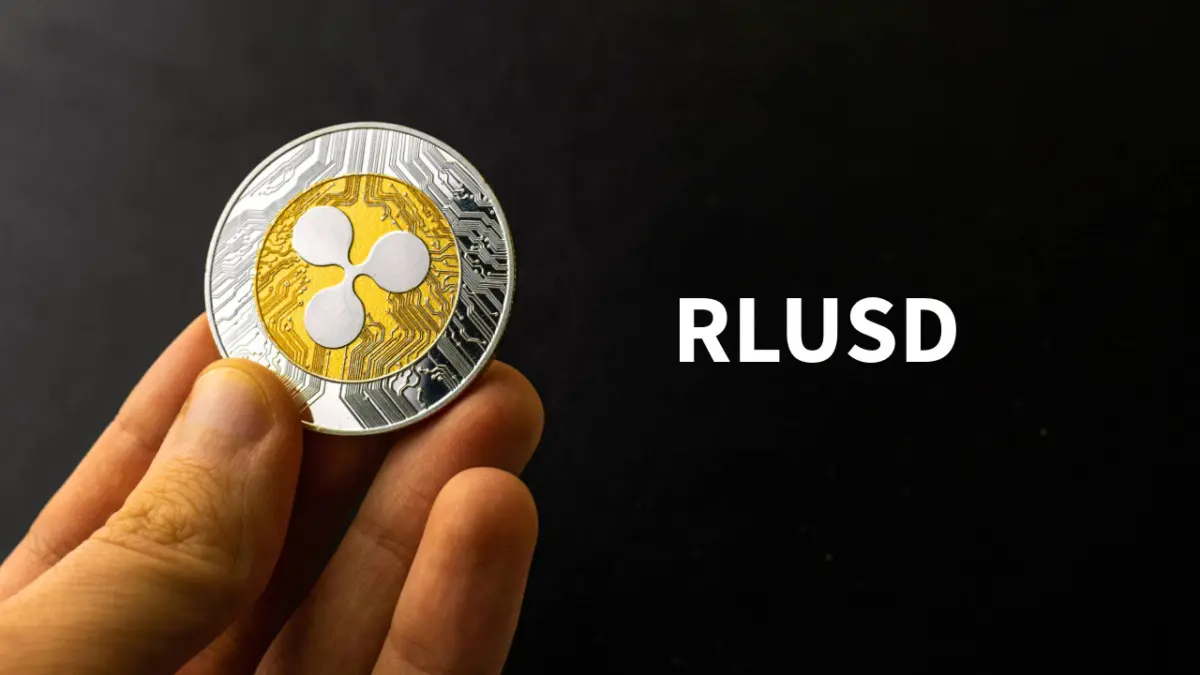 A hand holding a physical XRP token coin with the text RLUSD displayed on a black background
