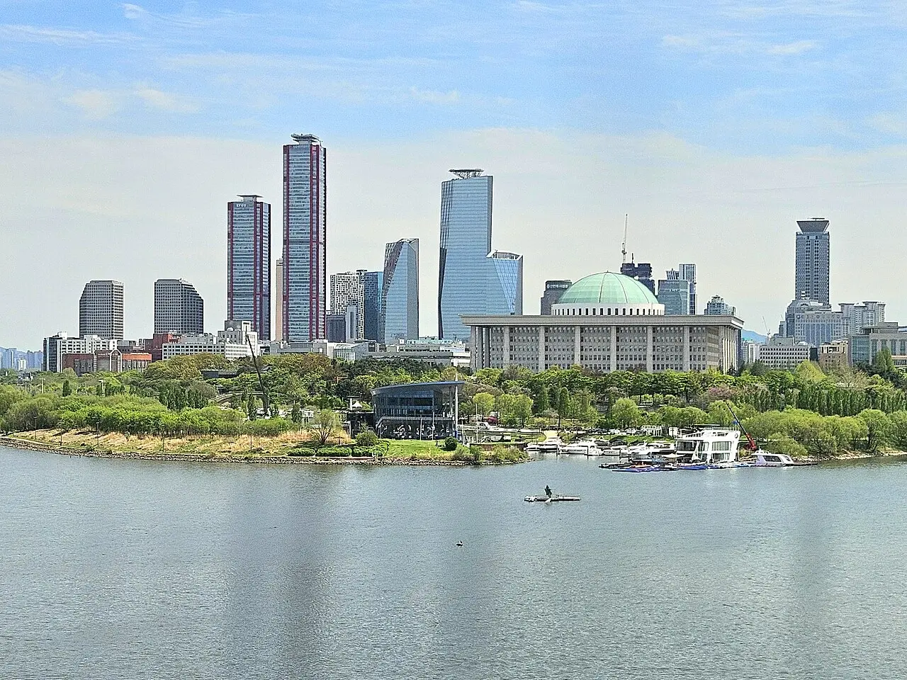 Wide shot of the Yeouido skyline in Seoul featuring modern skyscrapers and the National Assembly Building by the river.