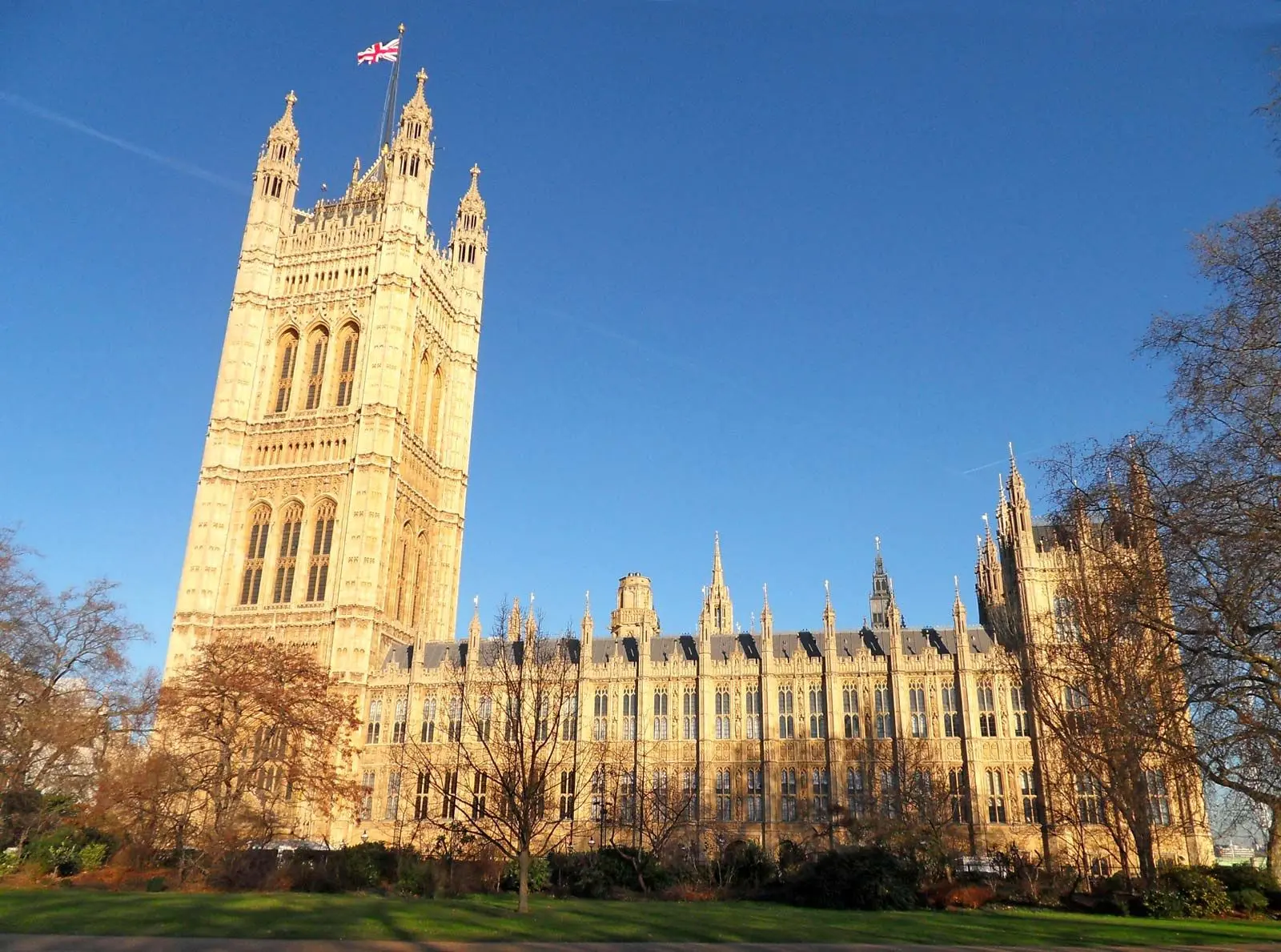 Palace of Westminster with the Union Jack flag flying against a clear blue sky.