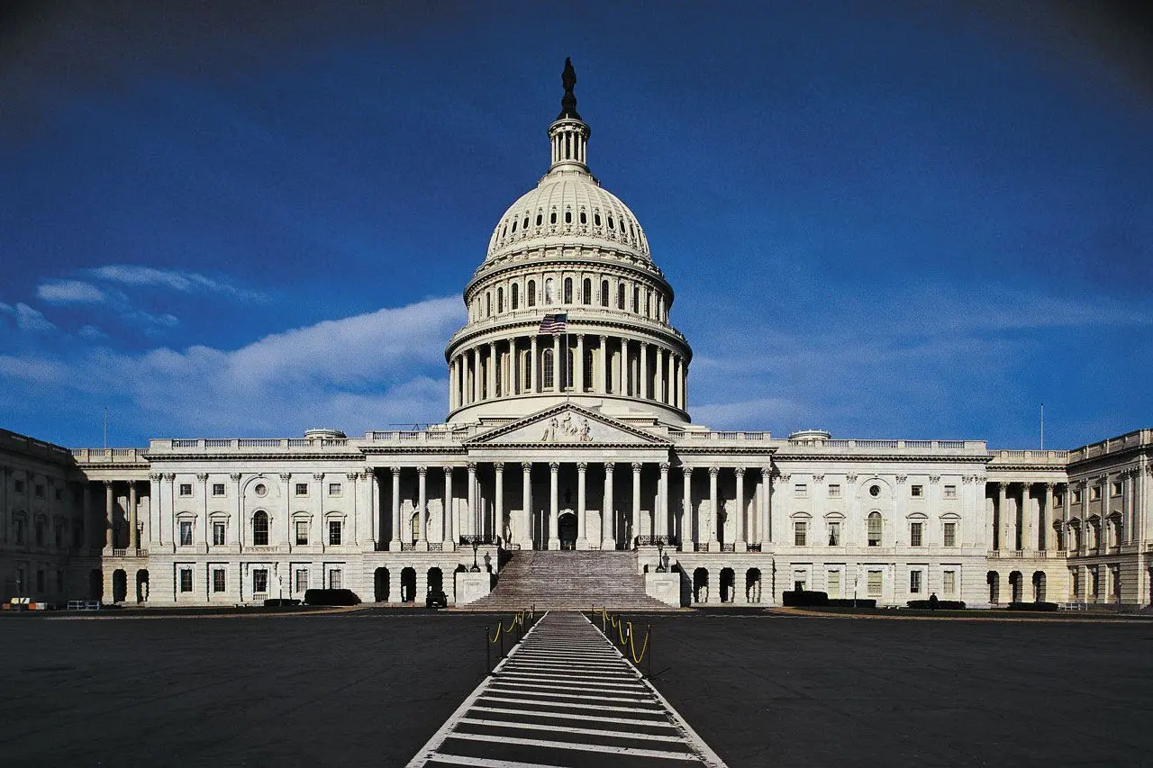 Front view of the United States Capitol building with its white dome and columns under a clear blue sky.