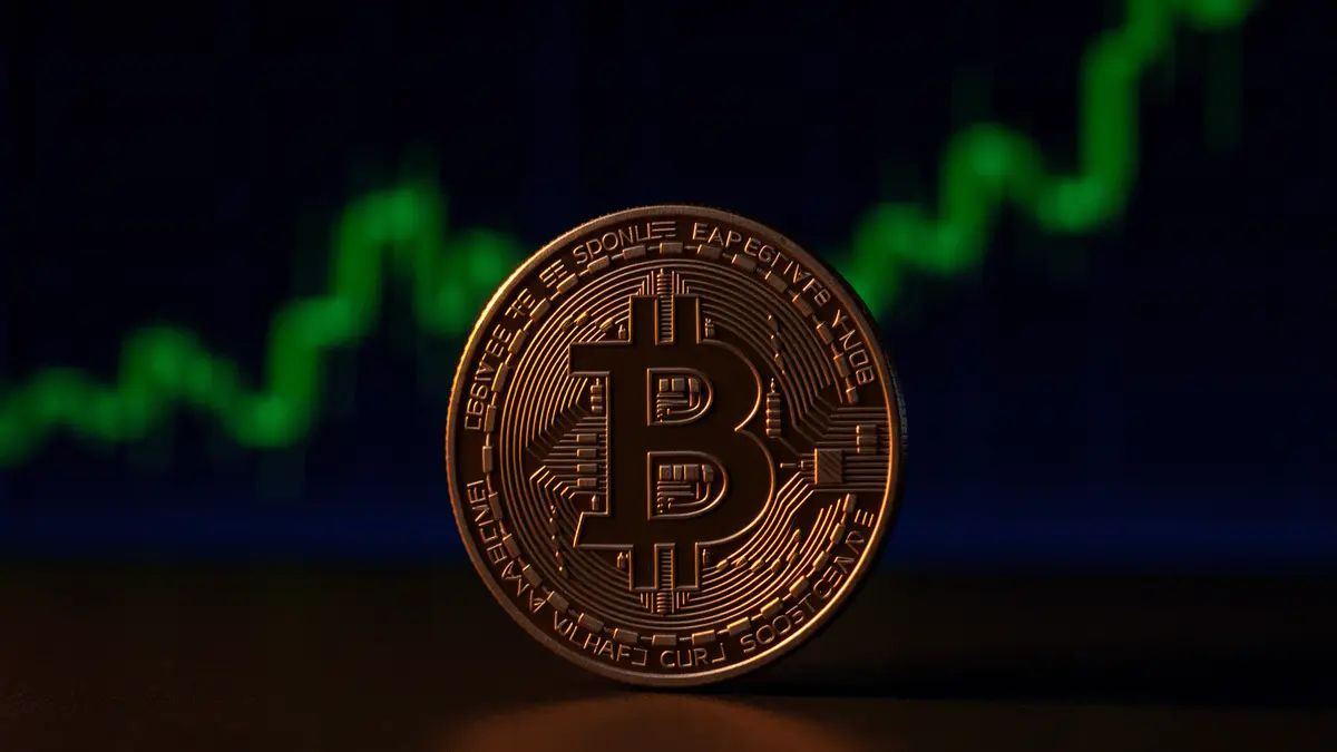 Bitcoin coin on dark surface with rising green chart in background