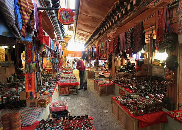 A narrow market alley in Thimphu, Bhutan, with traditional textiles and handicrafts displayed for sale.