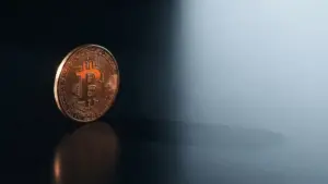 Bitcoin coin with dramatic lighting on black surface as liquidity drains away in cool blue background