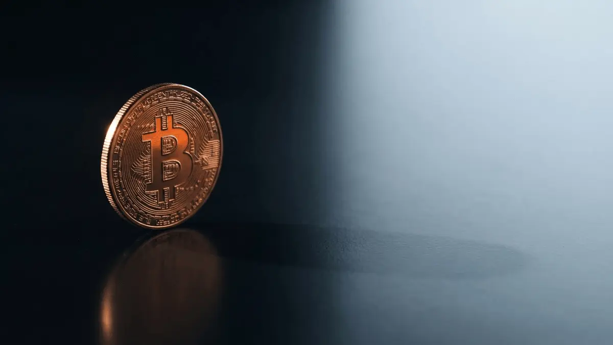 Bitcoin coin with dramatic lighting on black surface as liquidity drains away in cool blue background