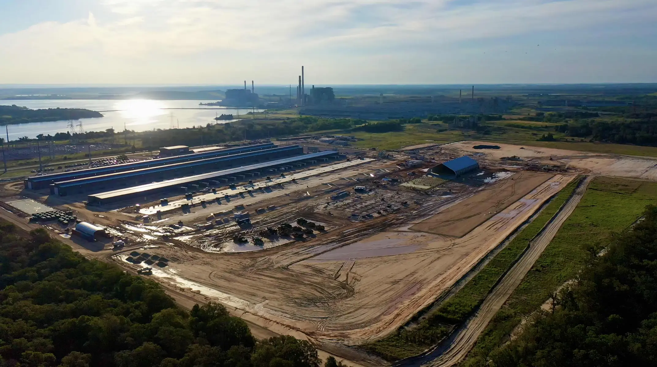 Aerial view of a large industrial complex with long metal sheds under construction in a muddy field