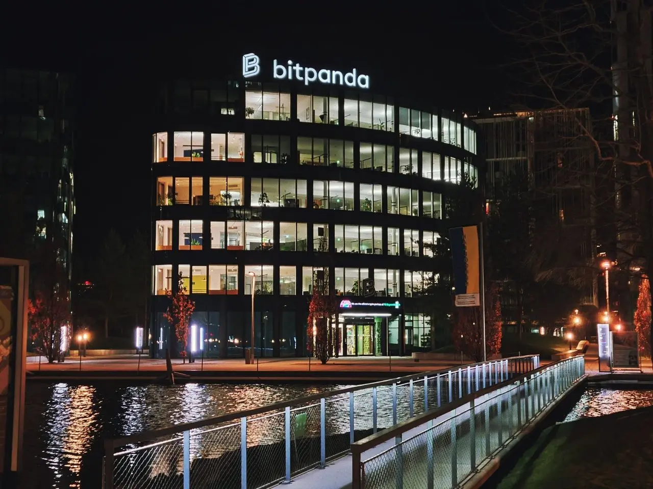Night view of the Bitpanda office building with its logo illuminated on the roof across a body of water