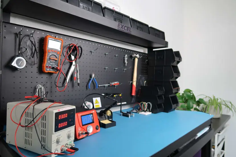 Electronics workbench with a digital multimeter, power supply, soldering tools, and a black pegboard organizer