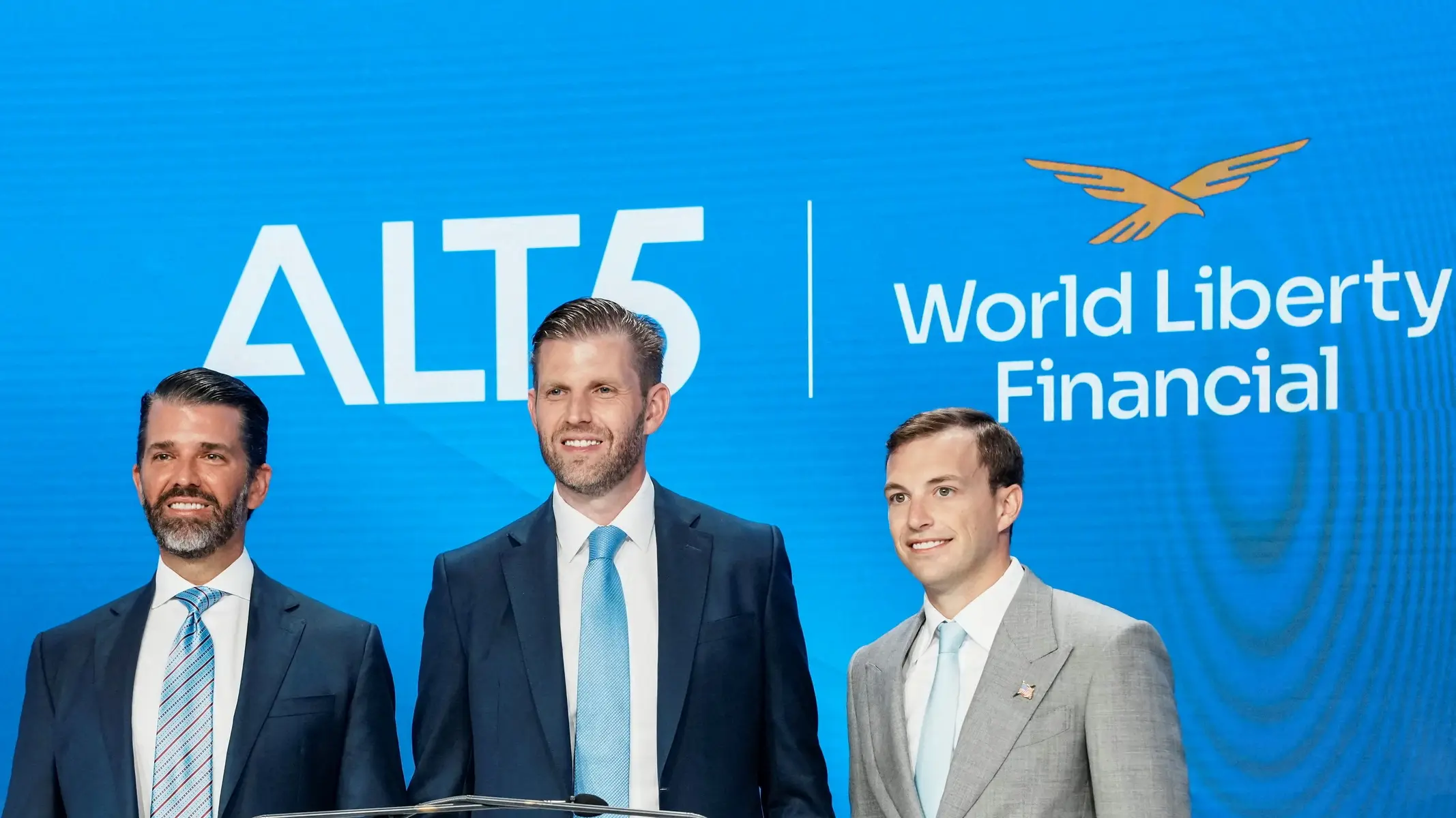 Three men in suits standing in front of a blue backdrop featuring the ALT5 and World Liberty Financial logos.