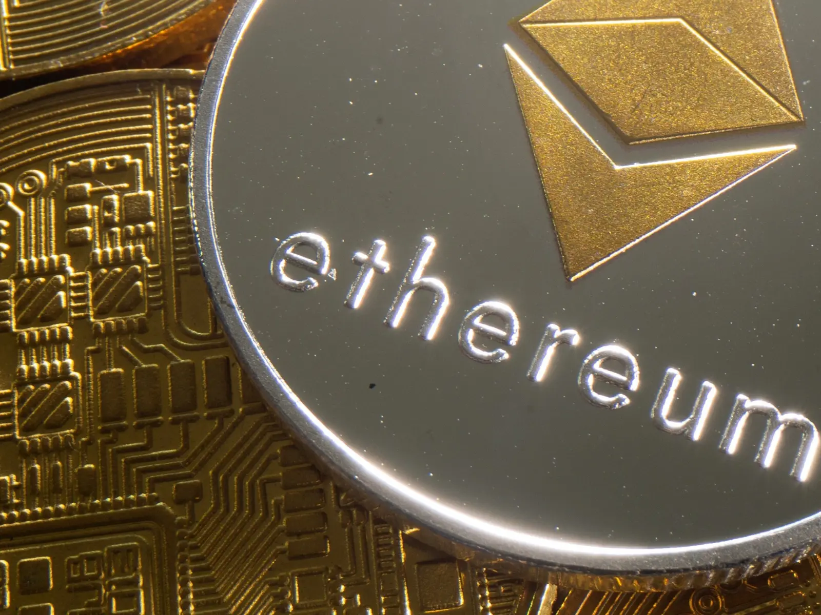 Close-up of a silver Ethereum coin with gold logo and text resting on gold circuit board patterns