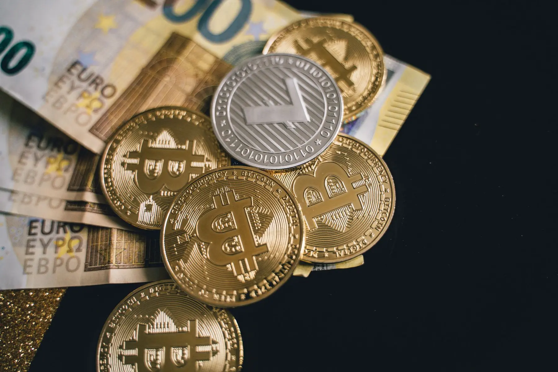 Gold Bitcoin and silver Litecoin coins resting on top of Euro banknotes