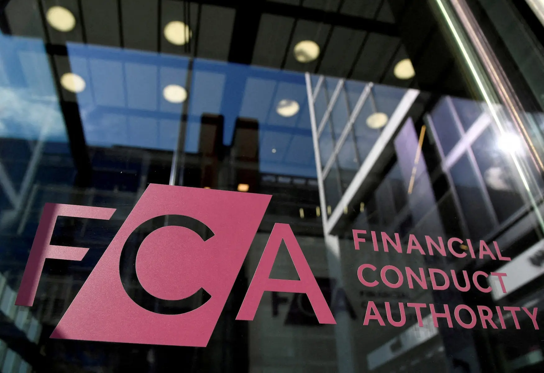 The Financial Conduct Authority (FCA) logo displayed on a glass window with reflections of city buildings.
