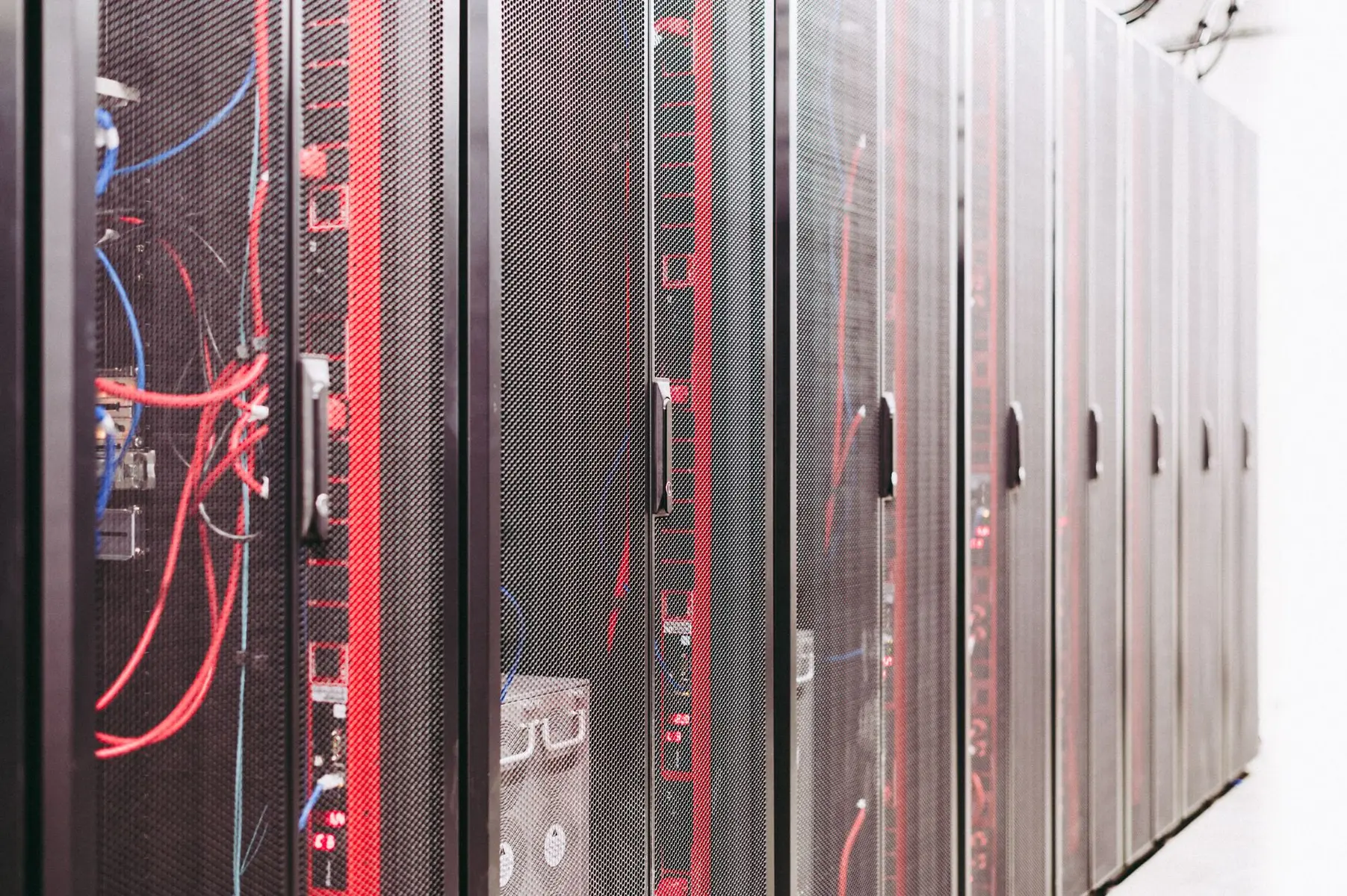A row of black server racks with mesh doors and visible red and blue cabling in a data center