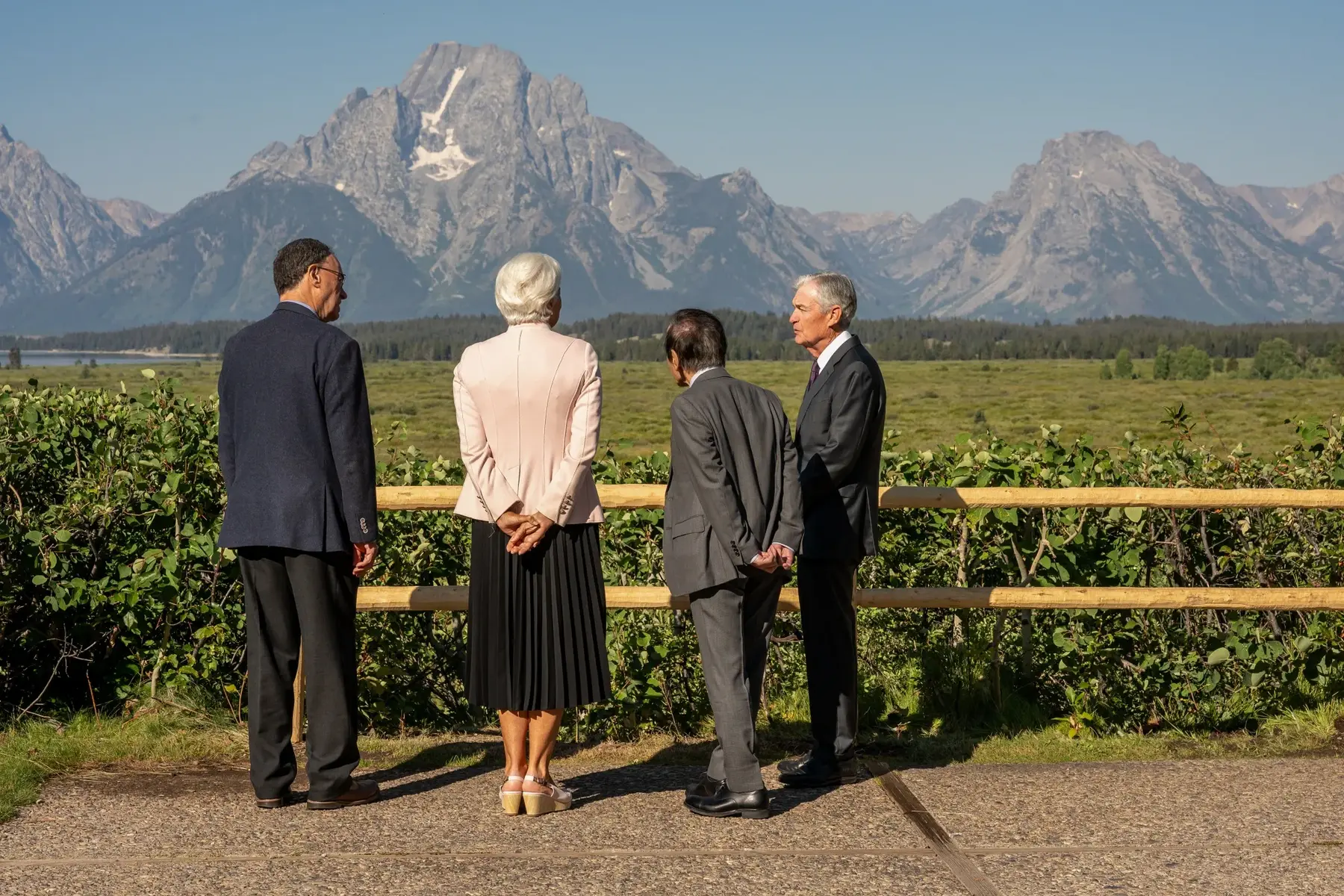 Four officials in business attire standing by a wooden fence looking at the Grand Teton mountains.