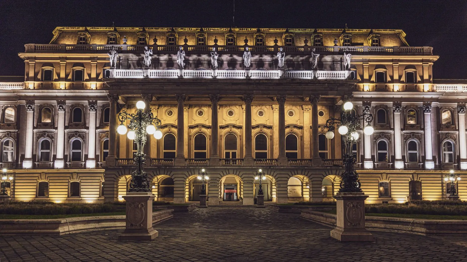 The illuminated neoclassical facade of the National Bank of Hungary building in Budapest at night.