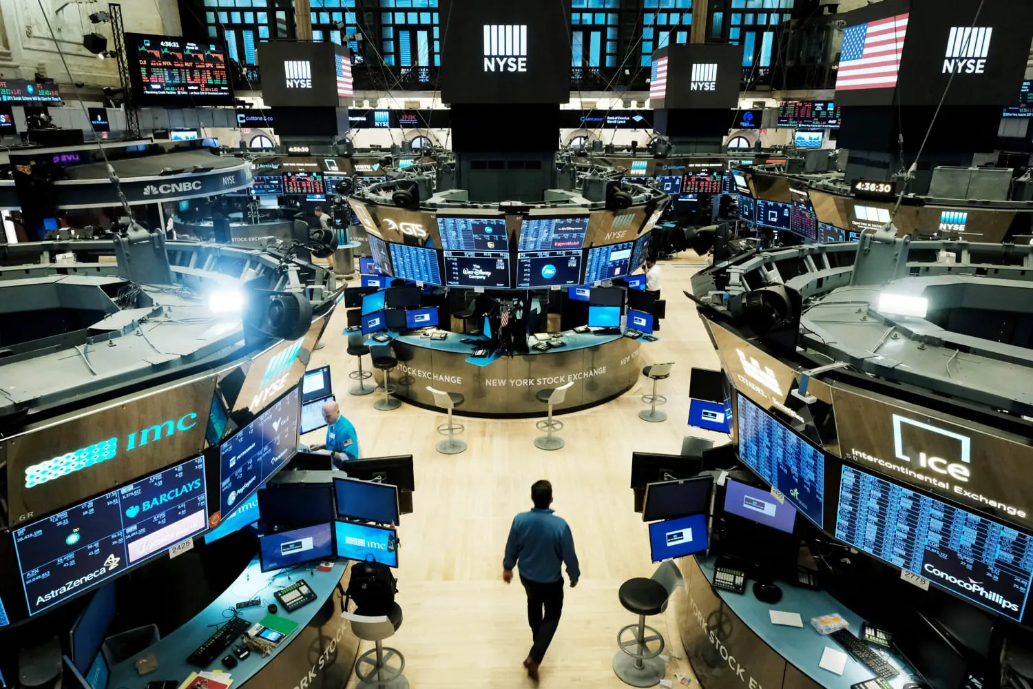 Wide shot of the New York Stock Exchange trading floor with multiple computer monitors, traders, and NYSE branding.