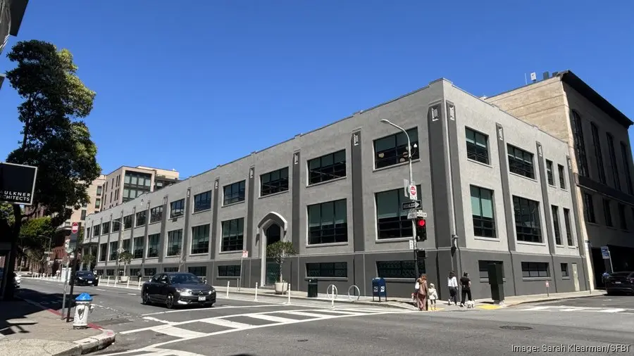 Exterior view of a gray multi-story office building on a city street corner under a clear blue sky