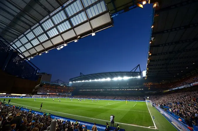 Wide view of a football match at Stamford Bridge stadium under a twilight sky