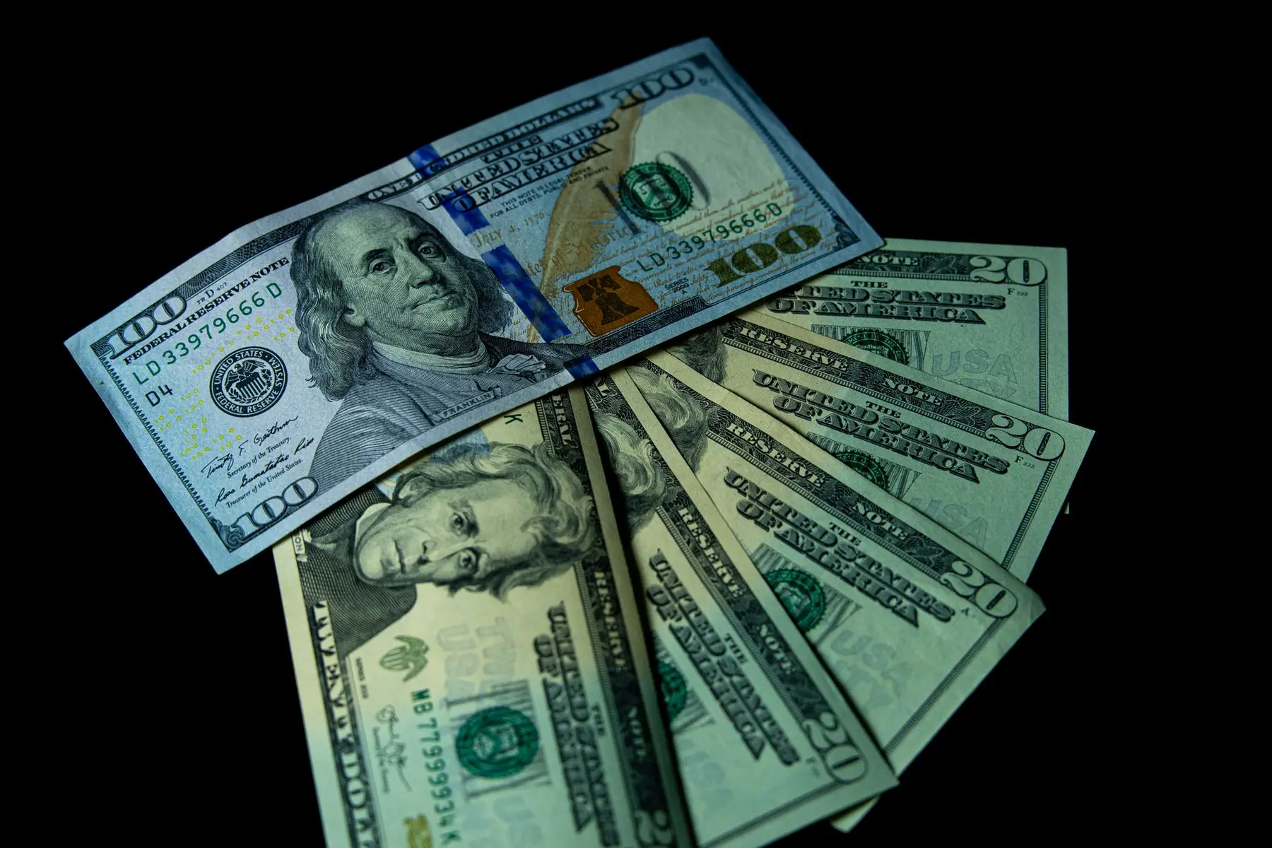 A stack of US dollar banknotes featuring one hundred and twenty dollar bills against a black background