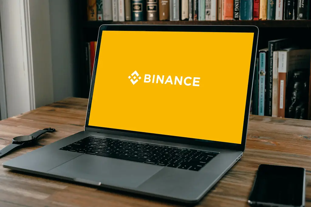 A laptop on a wooden desk displaying the yellow Binance logo and name on the screen.