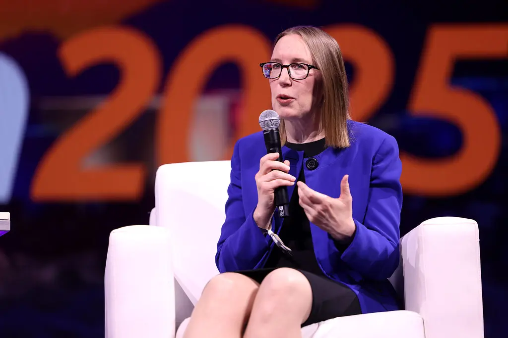 Hester Peirce speaking into a microphone while seated in a white chair during a panel discussion.