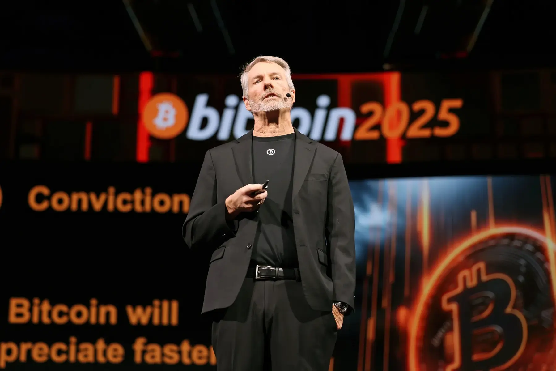 Michael Saylor speaking on stage at a Bitcoin 2025 event with a presentation screen behind him.