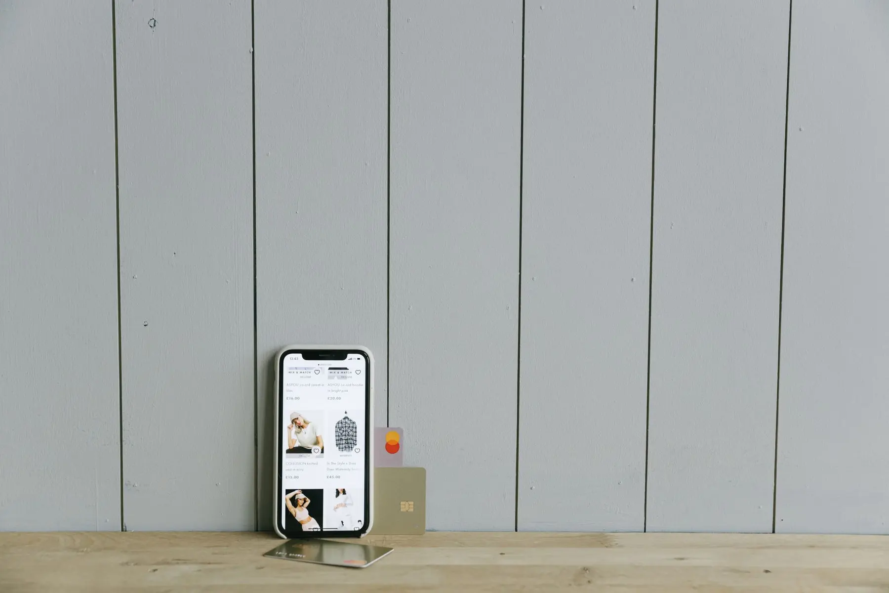 Smartphone displaying a shopping interface next to Revolut metal and plastic debit cards