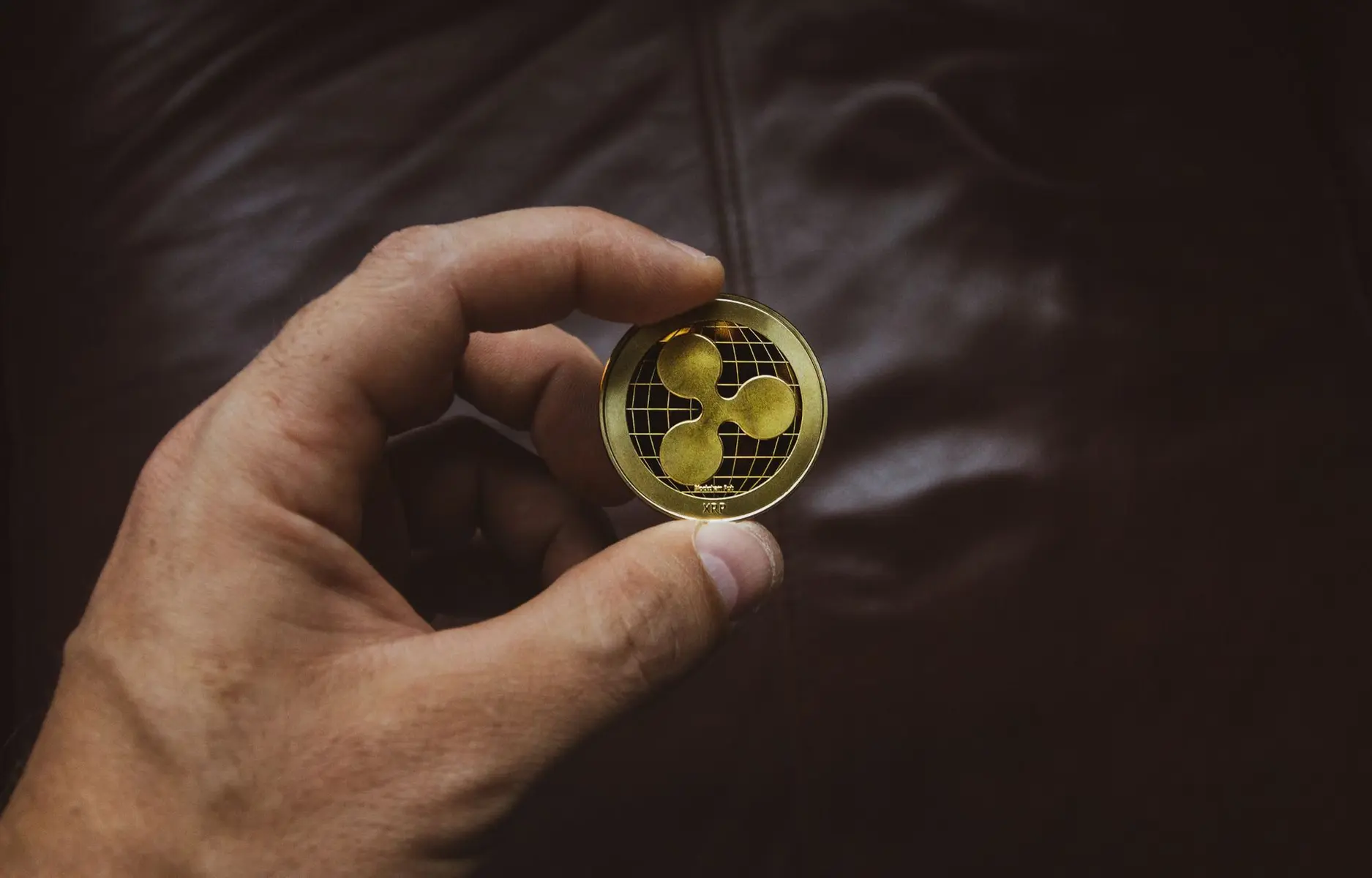 Close-up of a hand holding a physical gold XRP cryptocurrency token with the Ripple logo