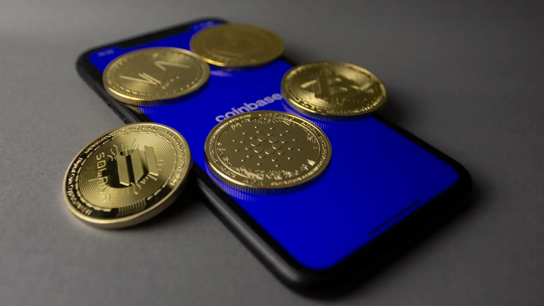 Gold cryptocurrency coins including Solana and Bitcoin resting on a smartphone screen with the Coinbase app open